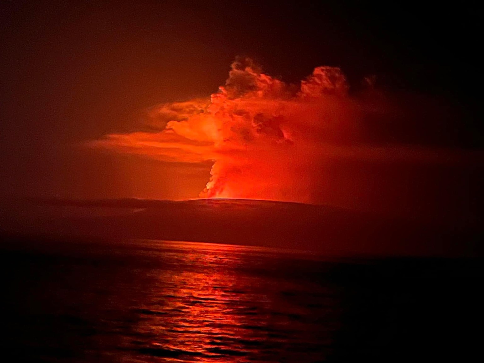 Glowing ash and lava explosion from an island in the ocean against a night sky