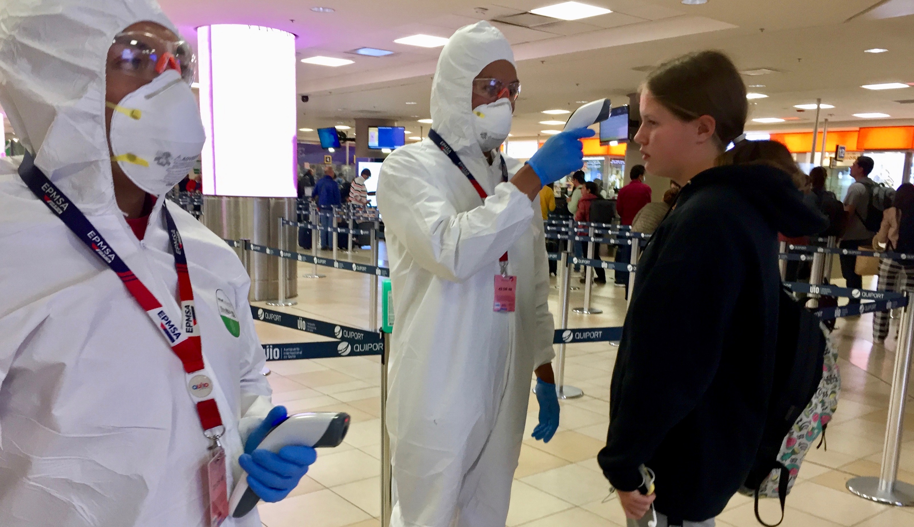 Teenage girl in black jumper having her temperature checked by man in white protective clothing in Quito airport