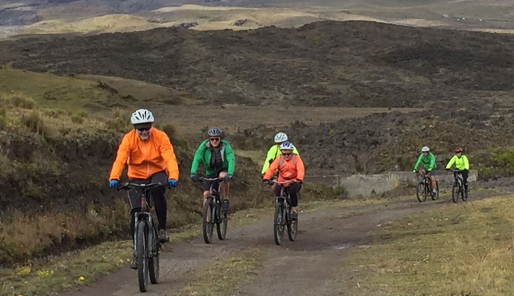 Group of six mountain bikers in neon jackets riding through countryside of Cotopaxi National Park, Ecuador