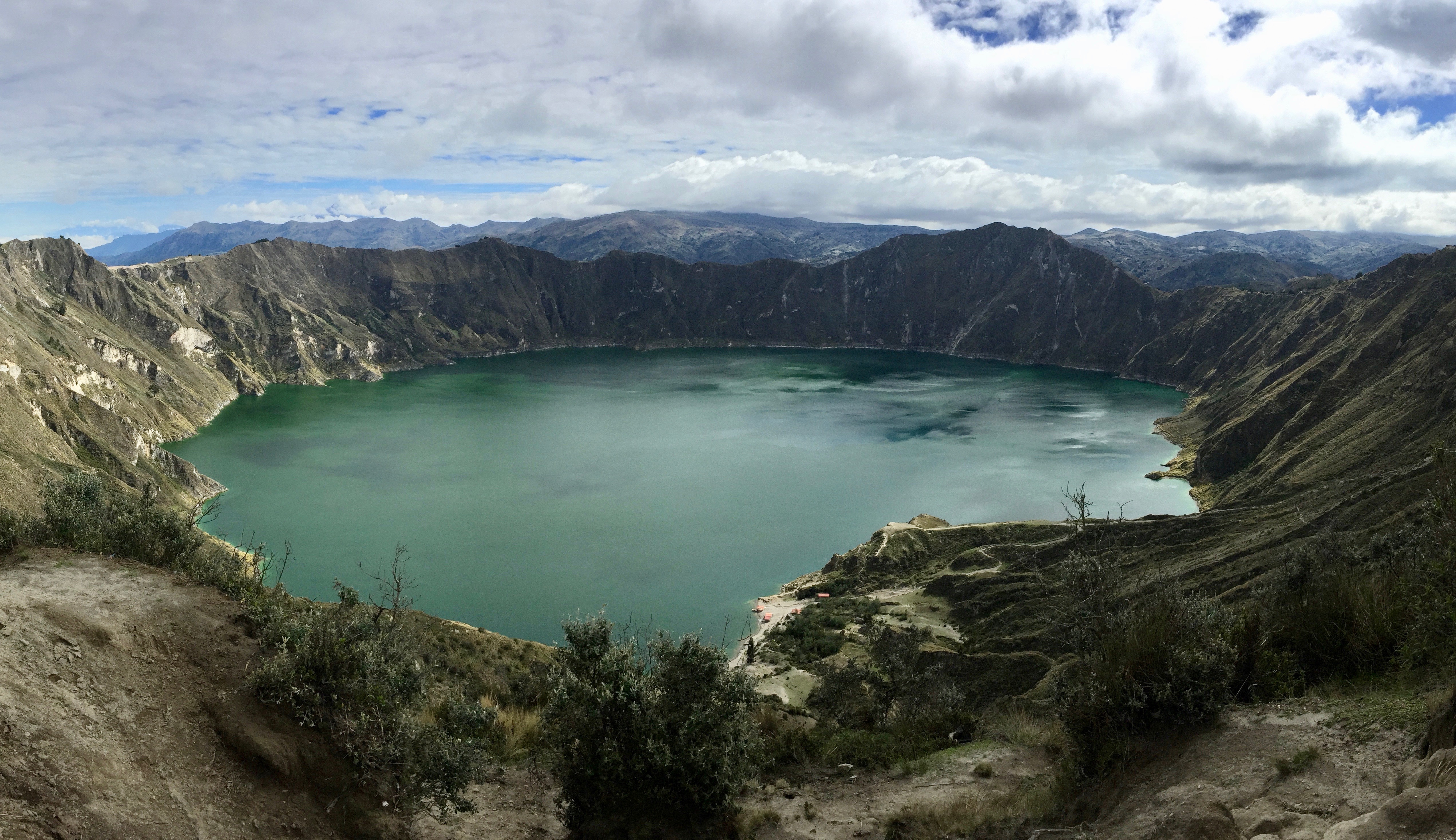 Blue green Quilotoa crater lake in grey green Andean mountains