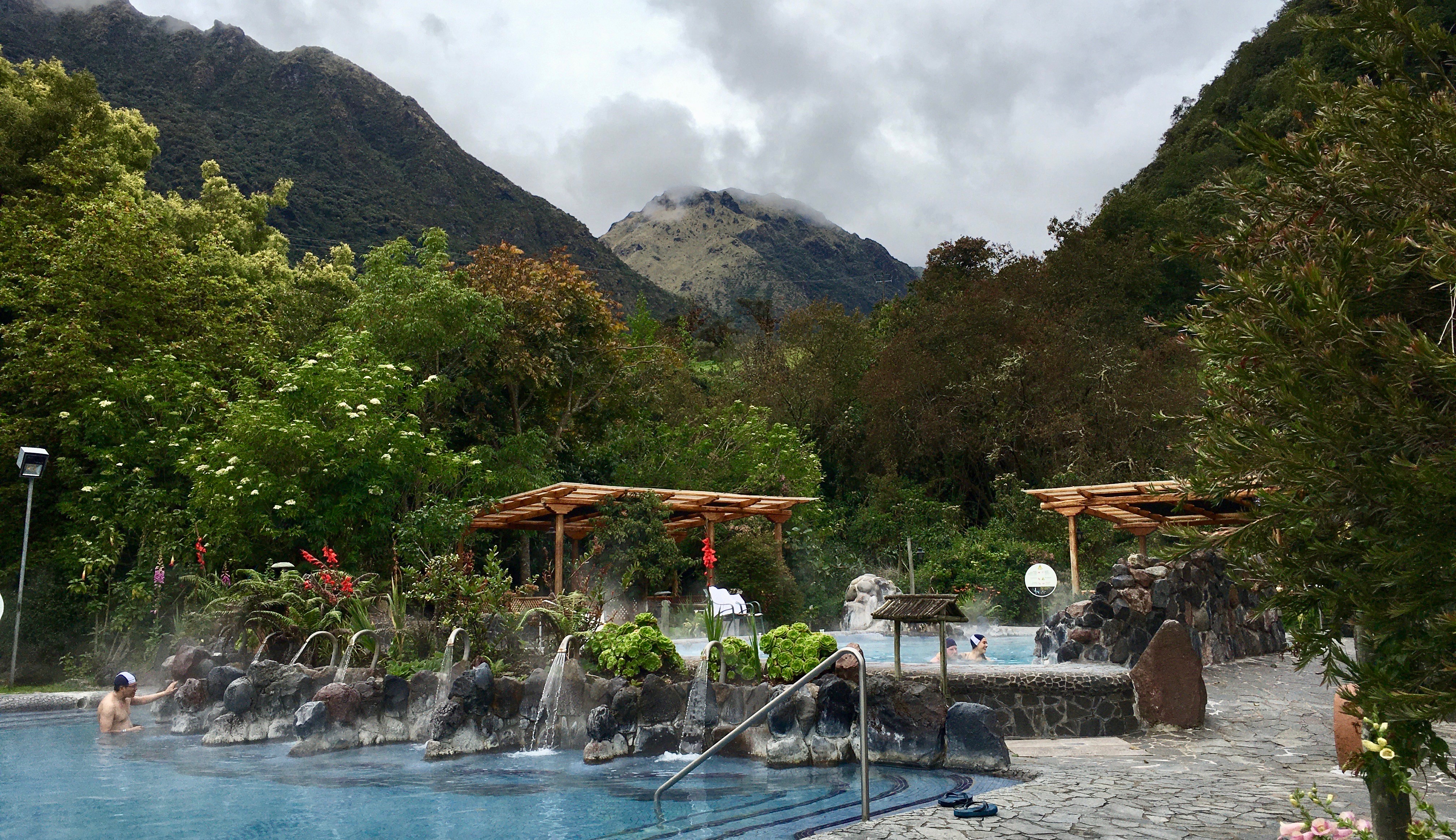 Thermal water pools in Papallacta, Ecuador with people bathing, surrounded by green vegetation, red flowers and high mountains