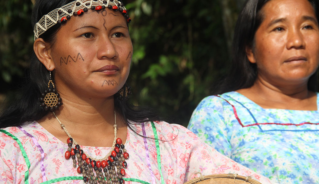 Two indigenous ladies, one with painted face, woven headdress, red and black seed necklace and pink top in Napo Cultural Center, Ecuador 