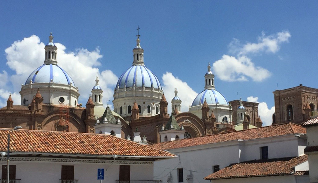 Three blue cupolas of the New Cathedral in Cuenca Ecuador rising above red tiled roofs of white washed buildings