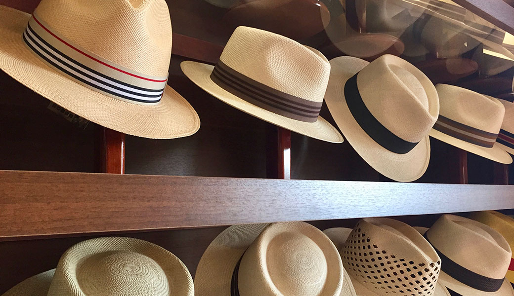 Two rows of Ecuadorian handmade Panama hats on a shop shelf in Cuenca, with brown and colourful bands