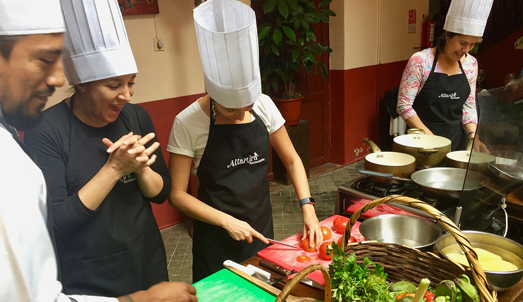 Woman with chef's hat and apron chopping tomatoes as friends and chef look on in Quito Cooking Class